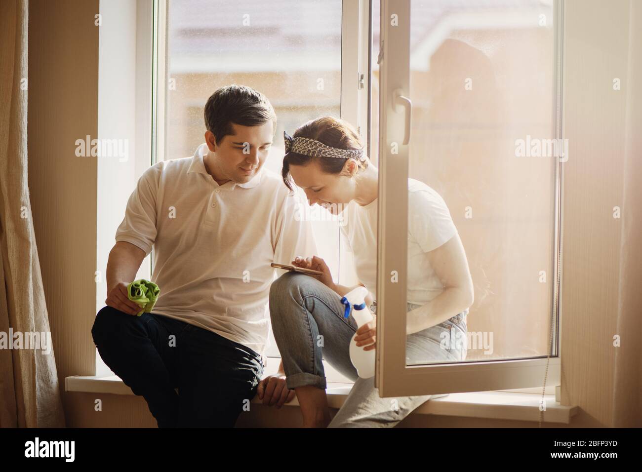 Young smiling couple is having rest after doing cleaning at home. Stock Photo