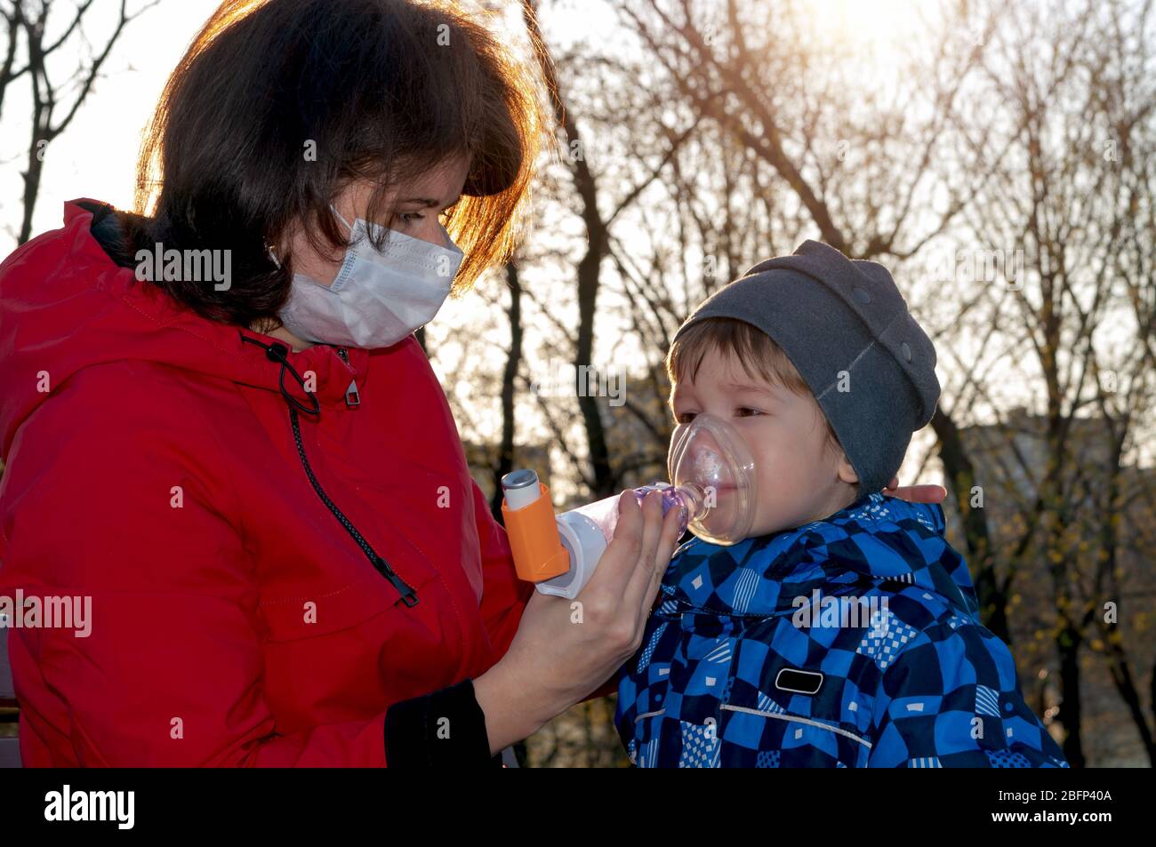 A small boy with illness bronchial asthma getting treatment with aerosol inhaler from his mama outdoors Stock Photo