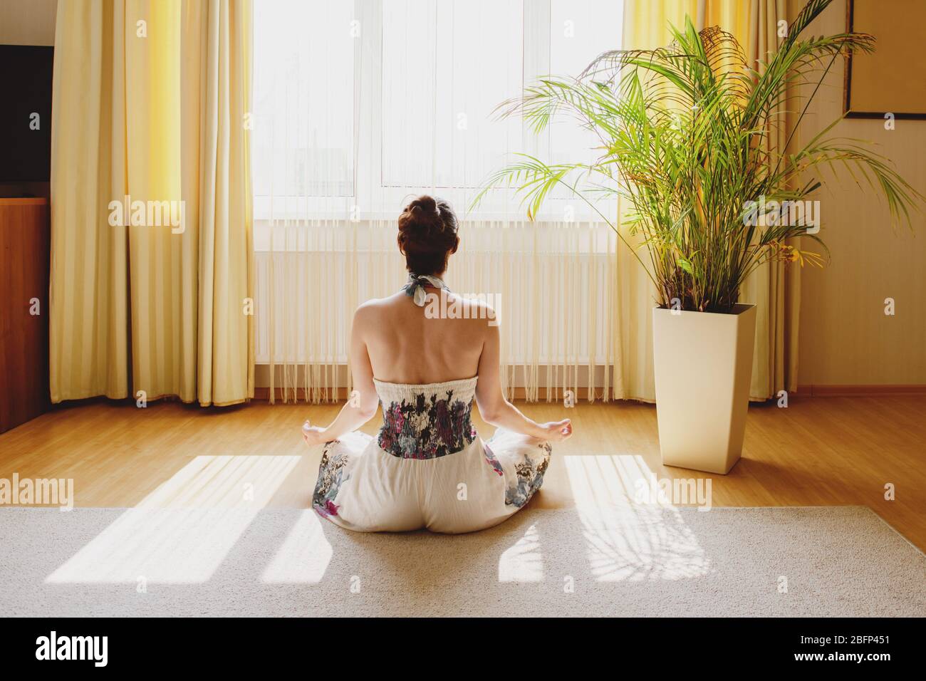 Back view of woman meditating on floor at home. Stock Photo