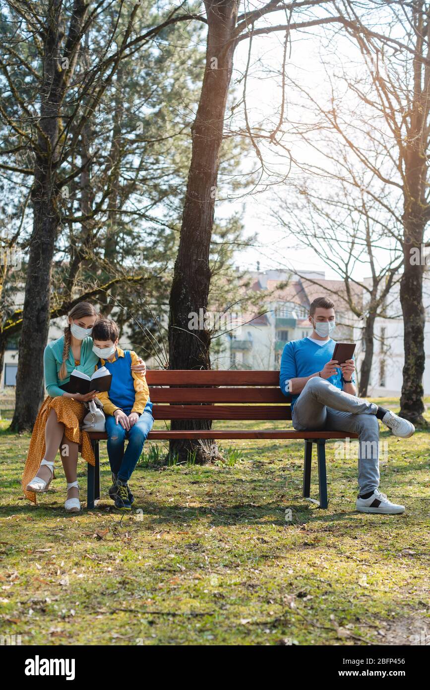 People sitting on park bench in the sun practicing social distancing Stock Photo