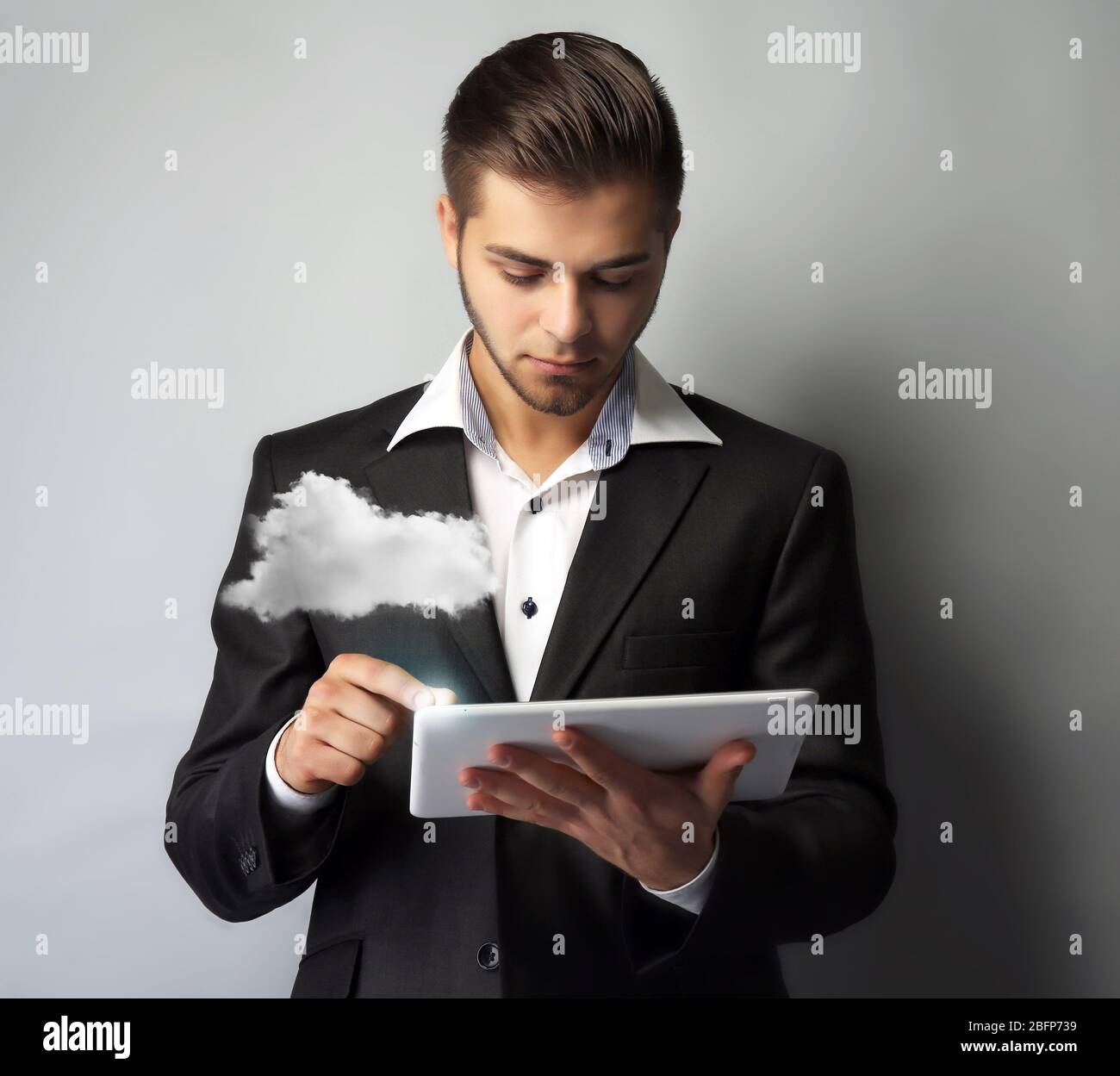 Businessman using tablet on gray background. Cloud computing and information storage concept. Stock Photo