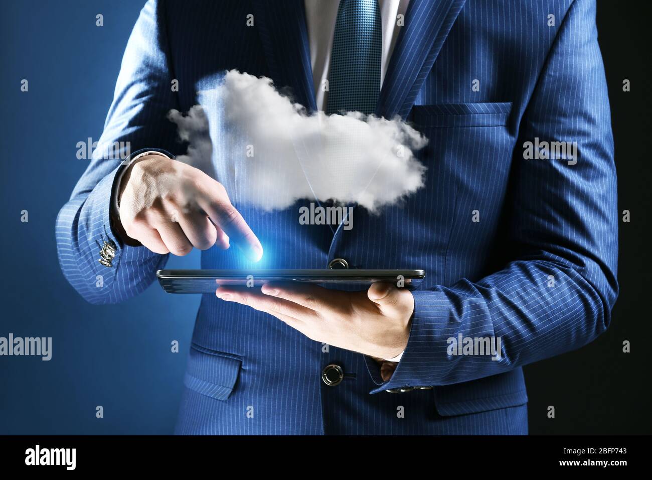 Businessman using tablet on blue background. Cloud computing and information storage concept. Stock Photo