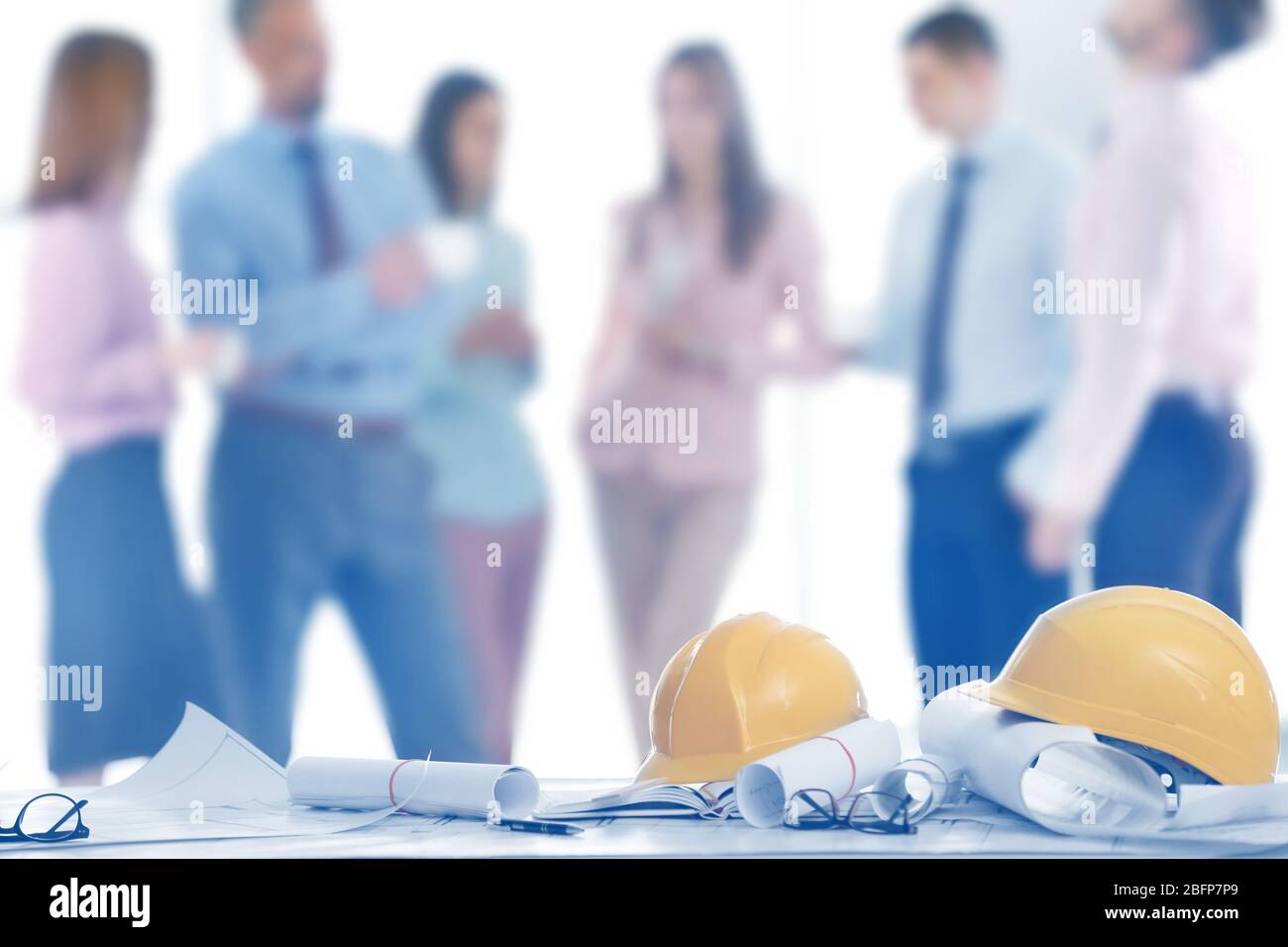 Helmets with blueprints on table and engineers on background Stock Photo
