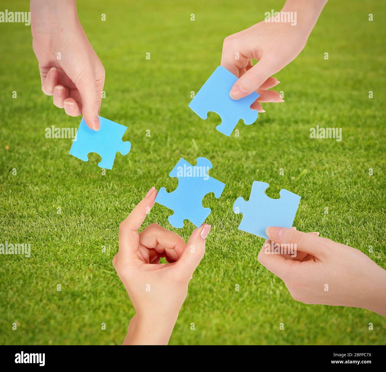 Hands with blue puzzle pieces on green grass background. Stock Photo