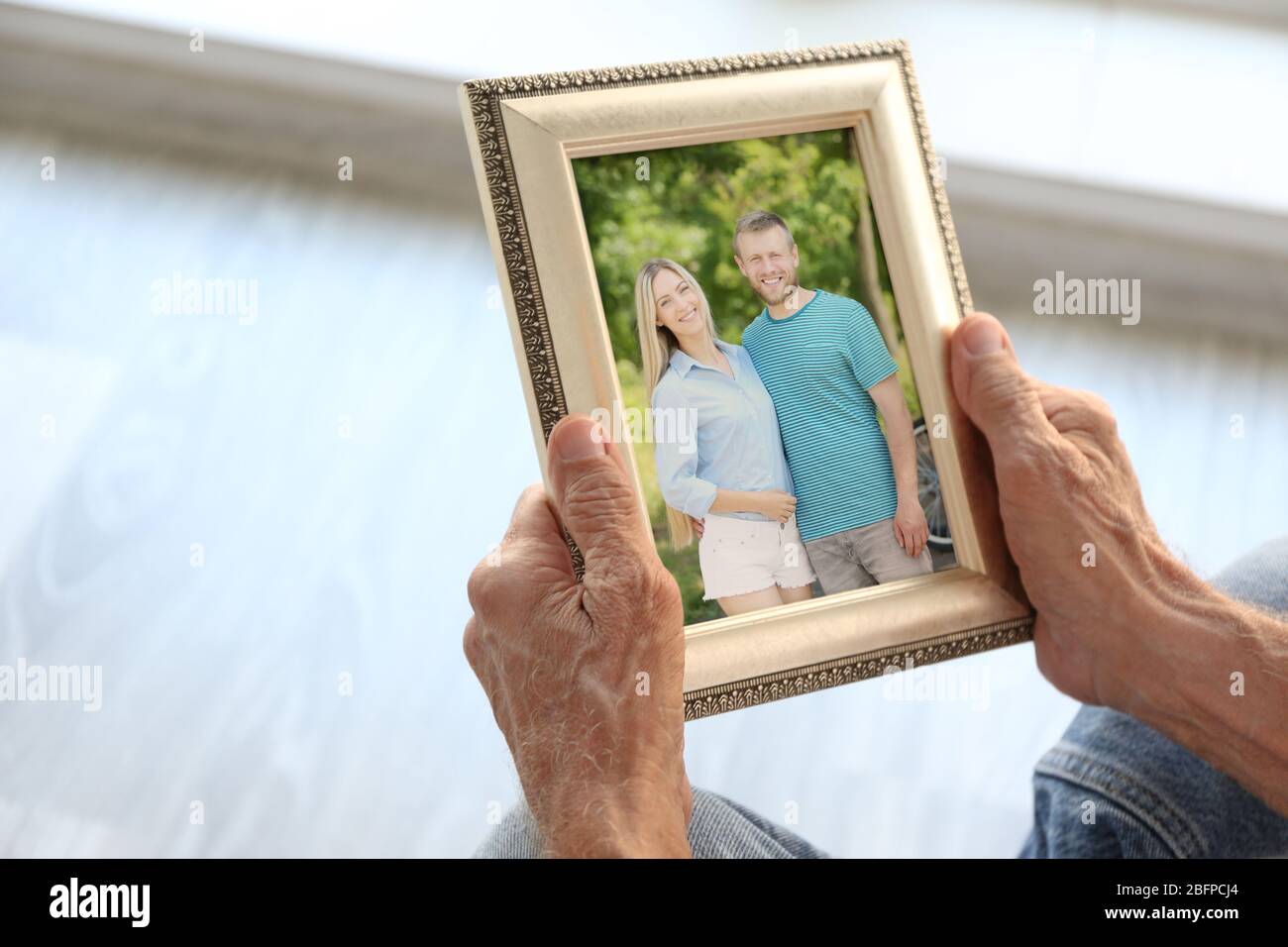 Elderly man holding photo frame with picture of young couple. Happy