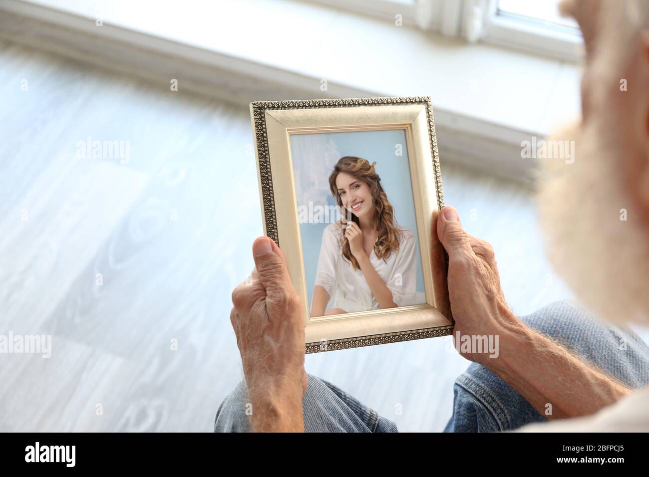 Elderly man holding photo frame with picture of young woman. Happy