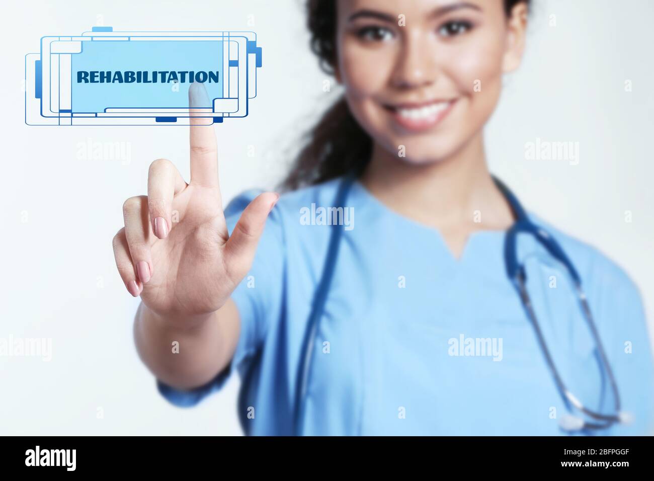 Recovery concept. Doctor pointing on word REHABILITATION against light background Stock Photo