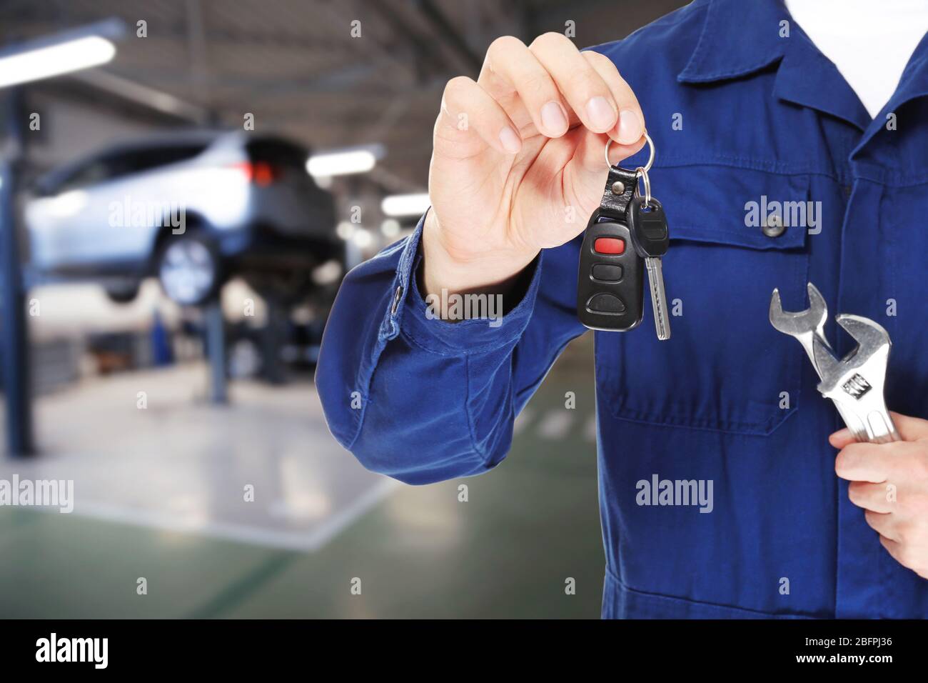 Auto mechanic holding key with tools and workshop on background. Car service concept Stock Photo