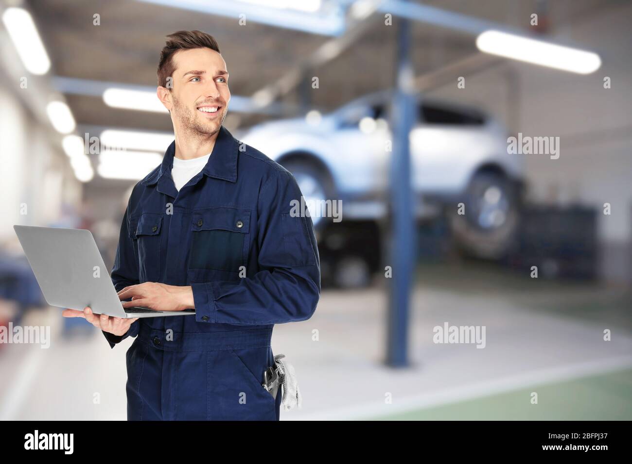 Auto mechanic with laptop and workshop on background. Car service concept Stock Photo