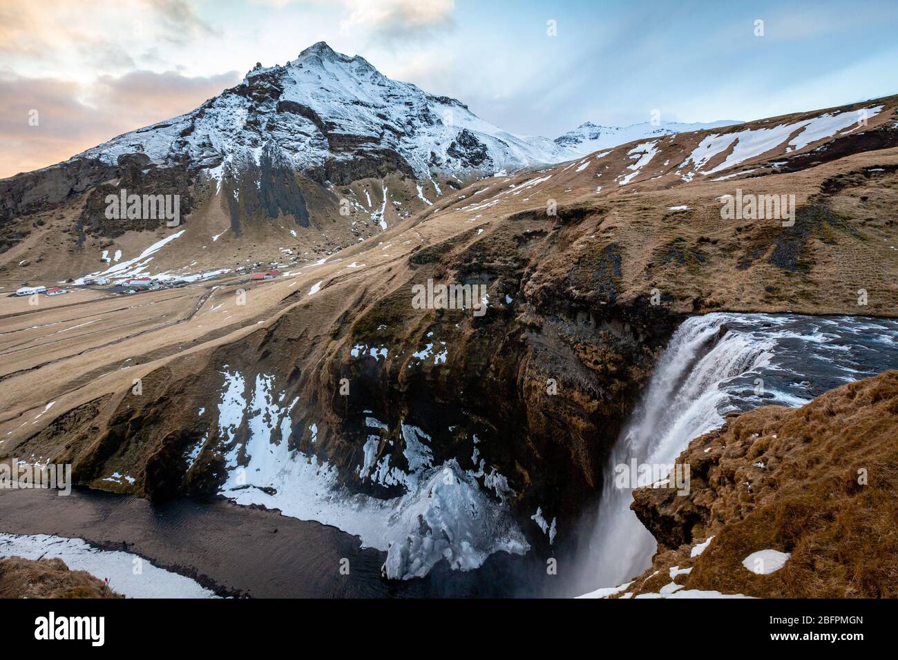 Looking down over the top of Skógafoss waterfall (Skogarfoss or Skogafoss)  the highest waterfall in Iceland in winter with a snow capped mountain Stock Photo