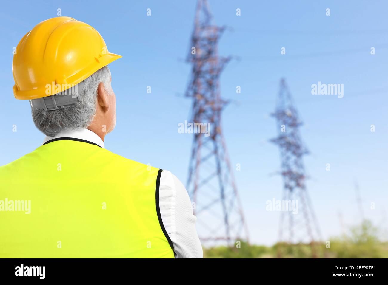 Senior engineer and electric transmission towers on background Stock