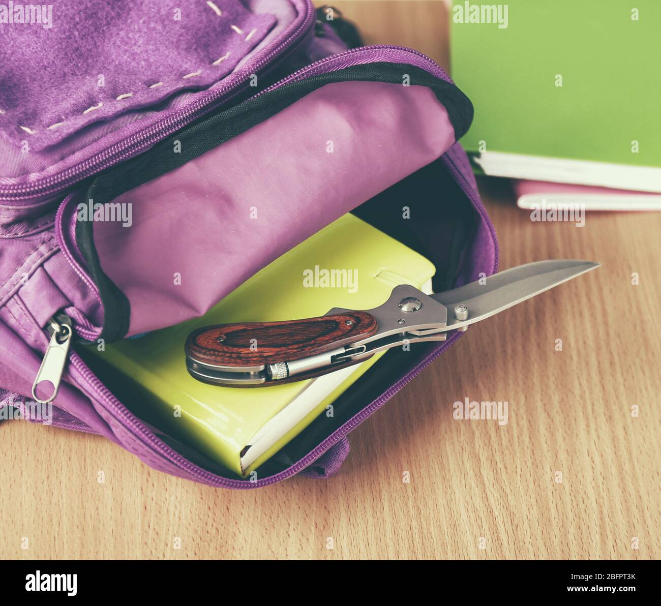 Backpack with knife on school desk in classroom, closeup Stock Photo