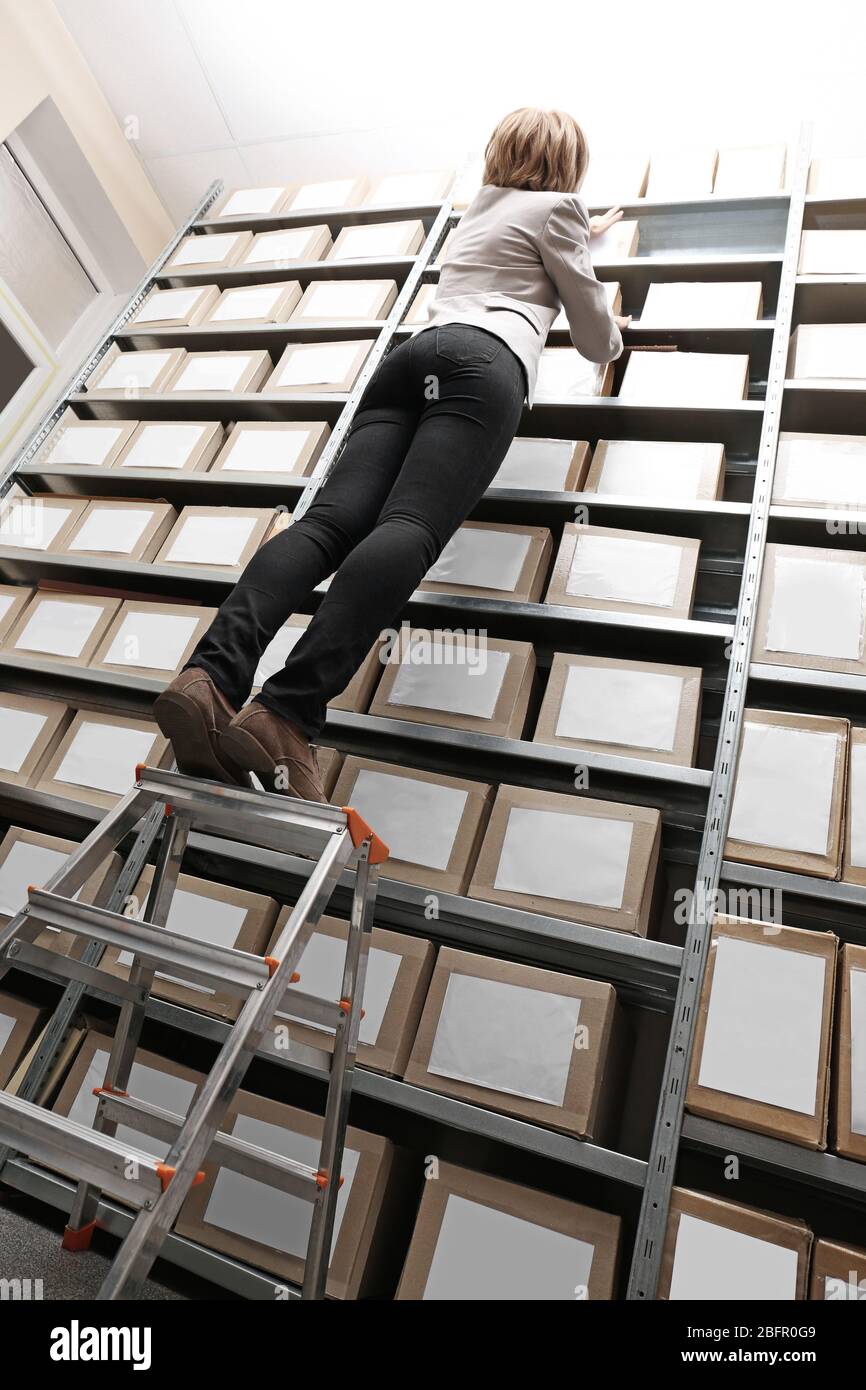 Woman standing on ladder while searching for documents in archive