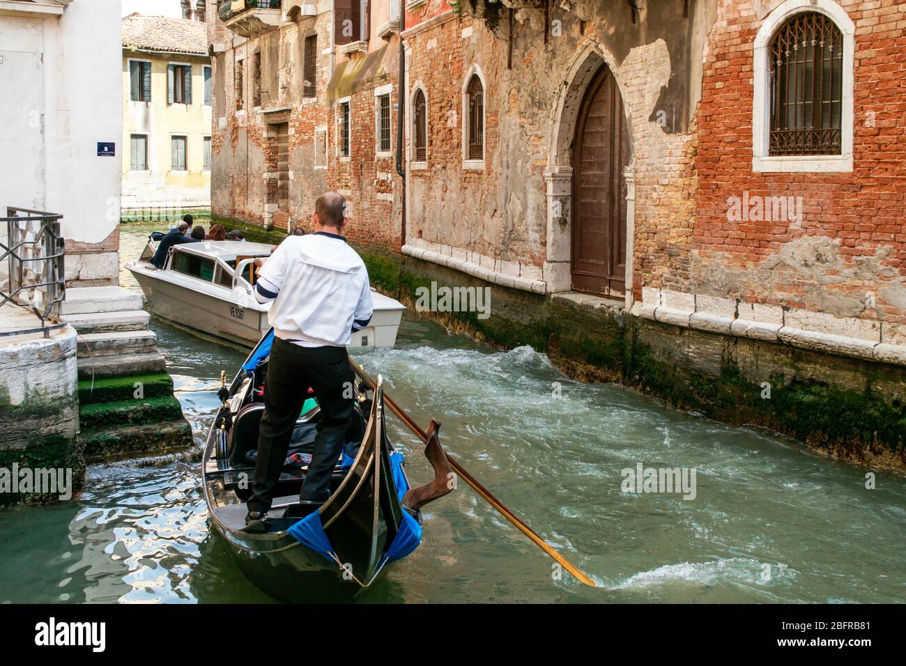 A gondolier moves his gondola to the side to allow a motorboat to pass. Venice, Italy Stock Photo