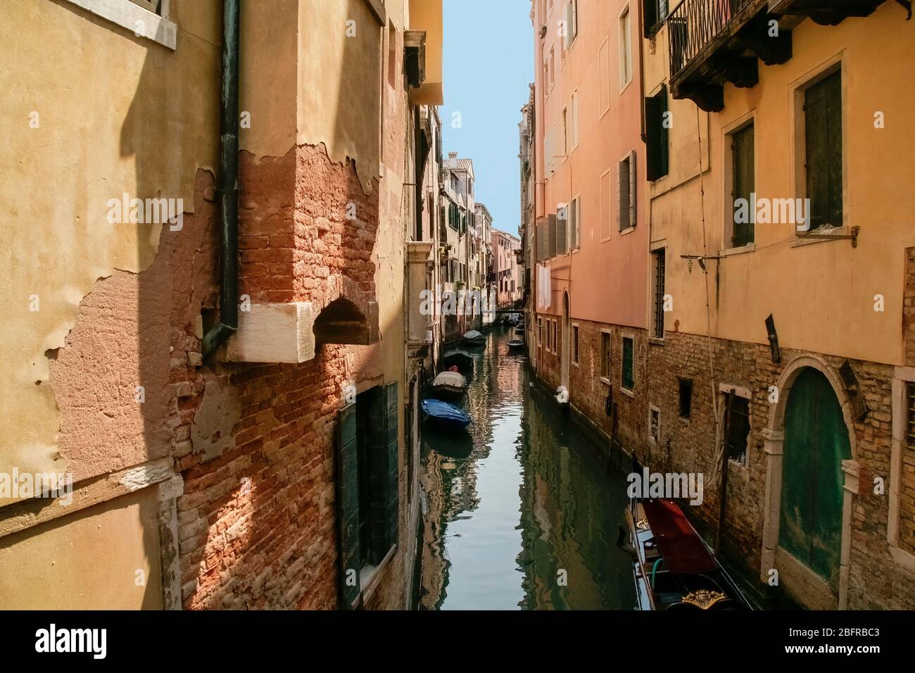 A narrow side canal between buildings with empty boats - no people. Venice Italy. Stock Photo