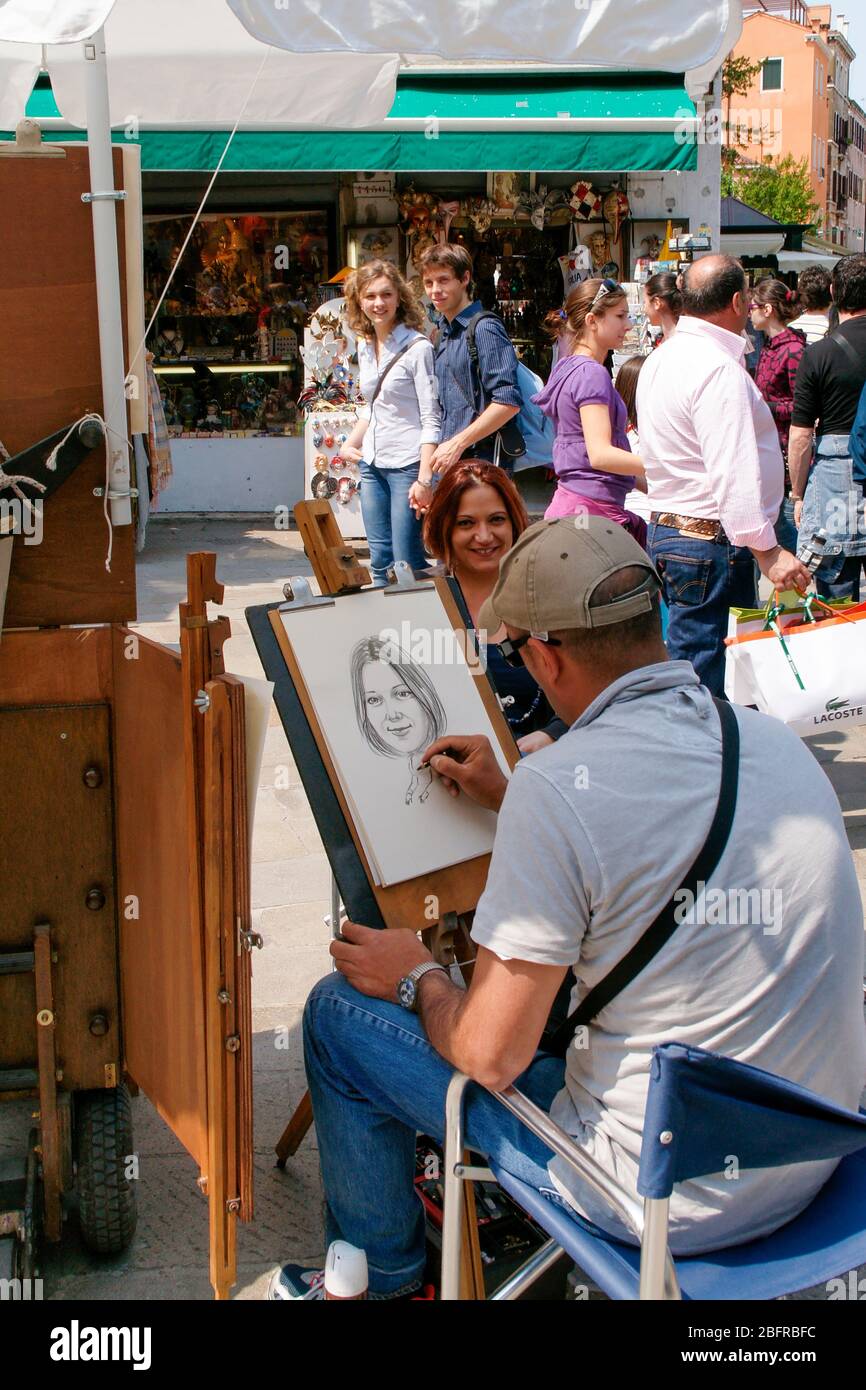 An artist drawsa portrait of a young woman as tourists walk by. Venice ...