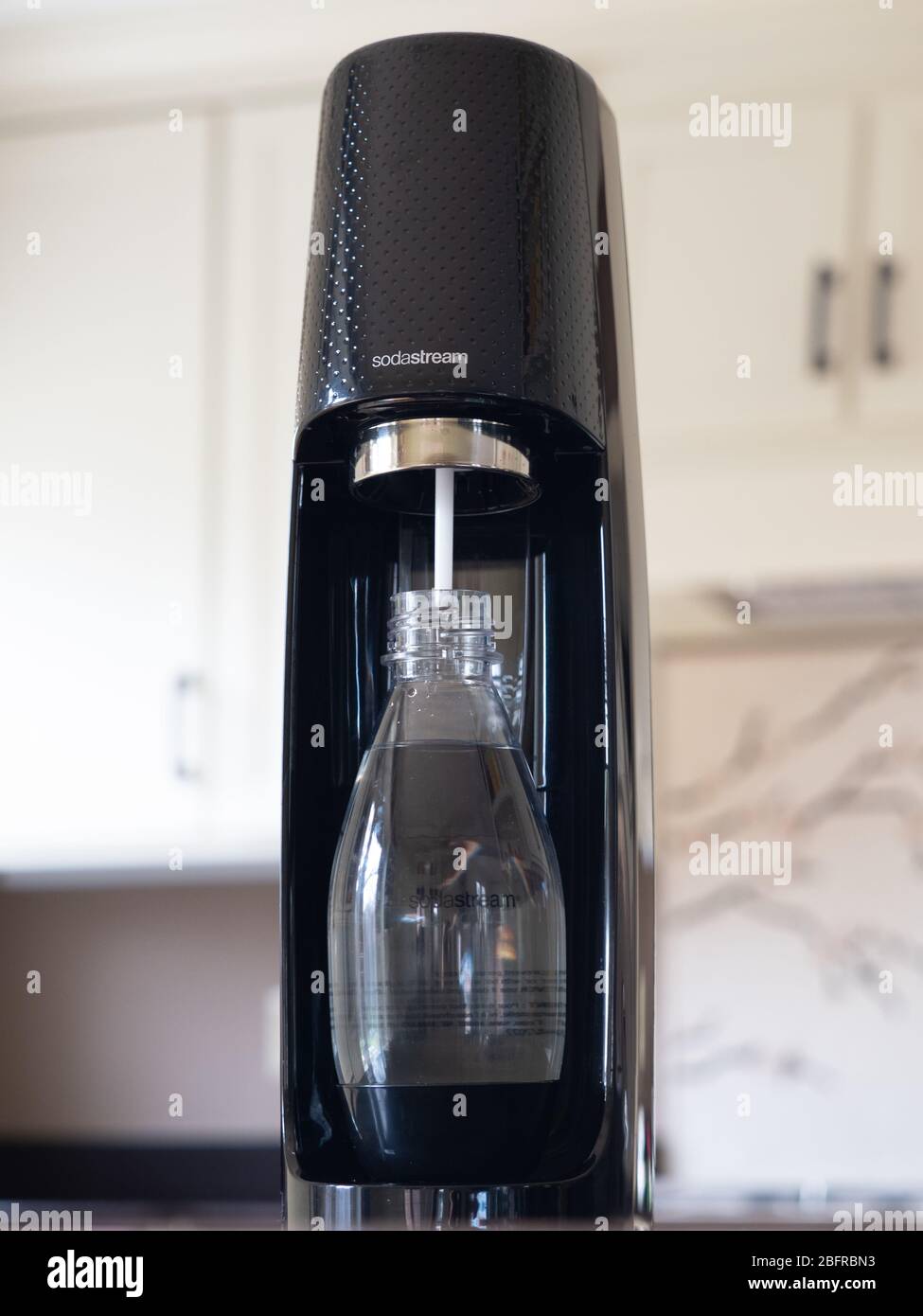 Black Sodastream carbonator and reusable Sodastream plastic bottle with water, photographed at eye level in modern kitchen with off white cabinets. Stock Photo