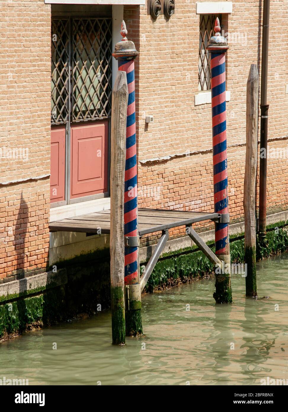 Traditional coloured striped mooring poles mark a building entrance from the canal. Venice, Italy Stock Photo