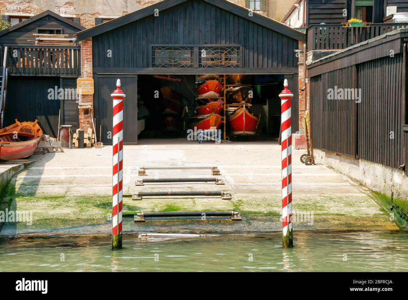 Red and white striped mooring poles mark the canal entrance to a boat storage business. Venice, Italy. no people Stock Photo