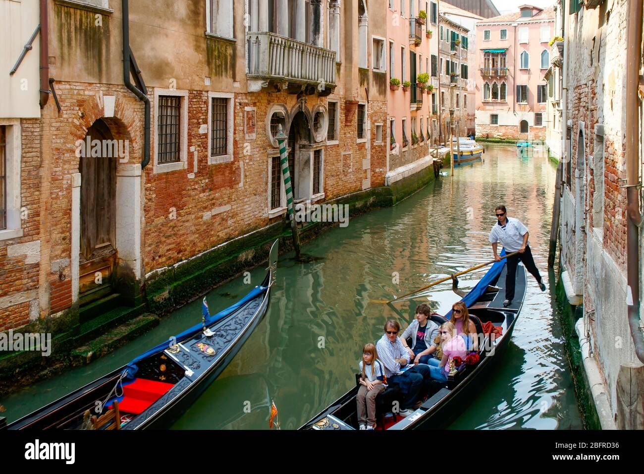 Two gondolas passing in a small side canal as the family riding in one looks at the surrounding buildings. Venice, Italy NMR Stock Photo