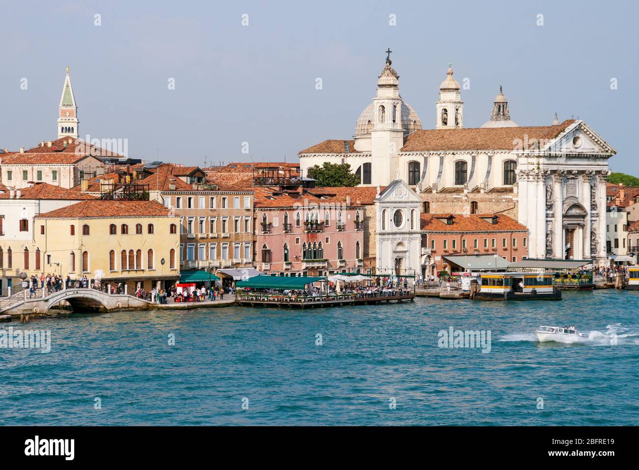 Walkway filled with people along the Grand Canal. Restaurants, hotels, residences and the Santa maria del Rosario church known as I Gesuati. Boats doc Stock Photo