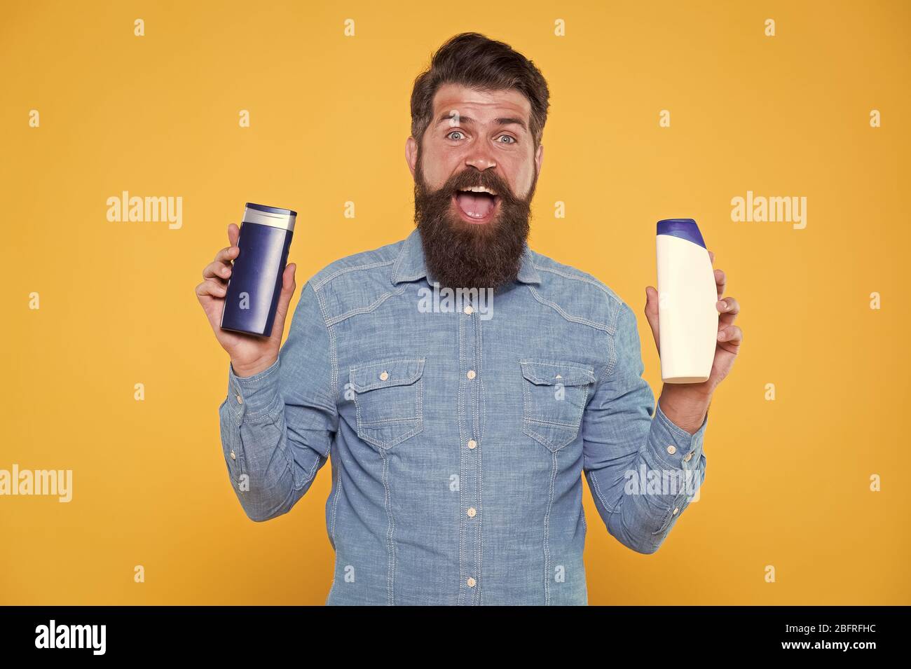 Grooming at every opportunity. Bearded man hold shampoo bottles yellow background. Cosmetics and