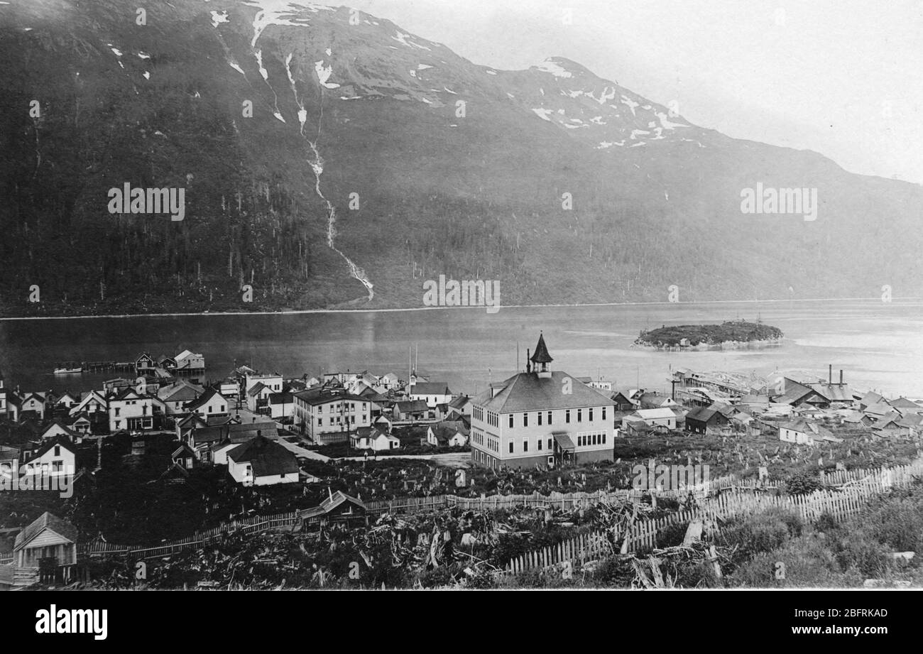 A view of the remote village of Douglas, on Douglas Island, in the Alaska Territory, 1907. The village sits beside the Gastineau Channel. Quite close across that channel in Juneau Alaska. The large building at the center was a school. Probably only a few hundred people lived here. A few years later, a long bridge was built connecting the village to the small island at right.   To see my other Places-related vintage images, Search:  Prestor  vintage  places  west Stock Photo