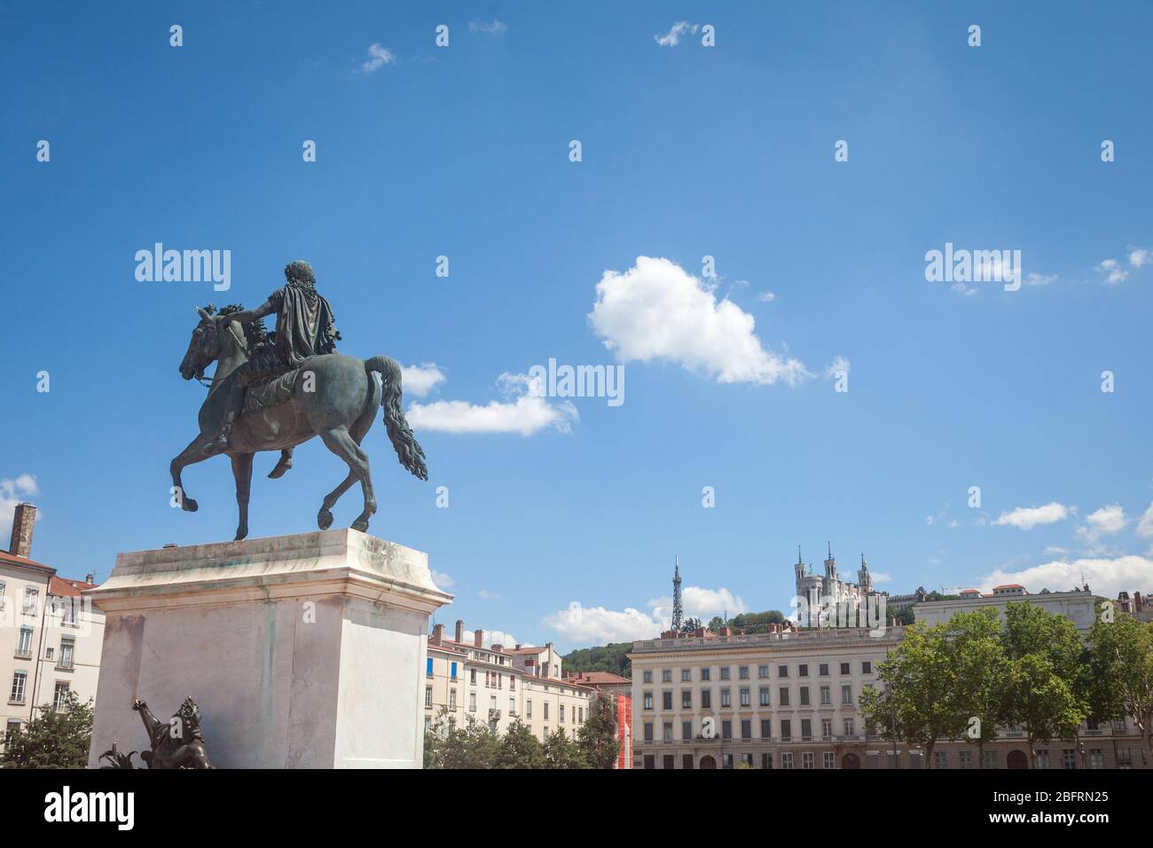 Roi Louis XIV statue on the Place Bellecour Square, in downtown Lyon, with the Basilique Notre Dame de Fourviere Church in background in summer. pict Stock Photo