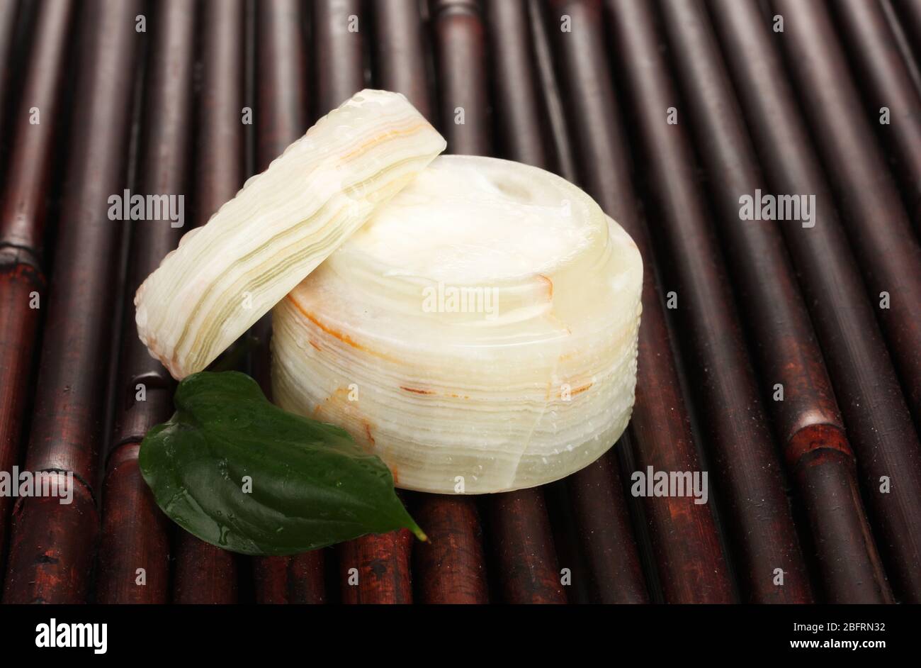 Opened jar of cream with fresh green leaf on bamboo mat with water droplets Stock Photo