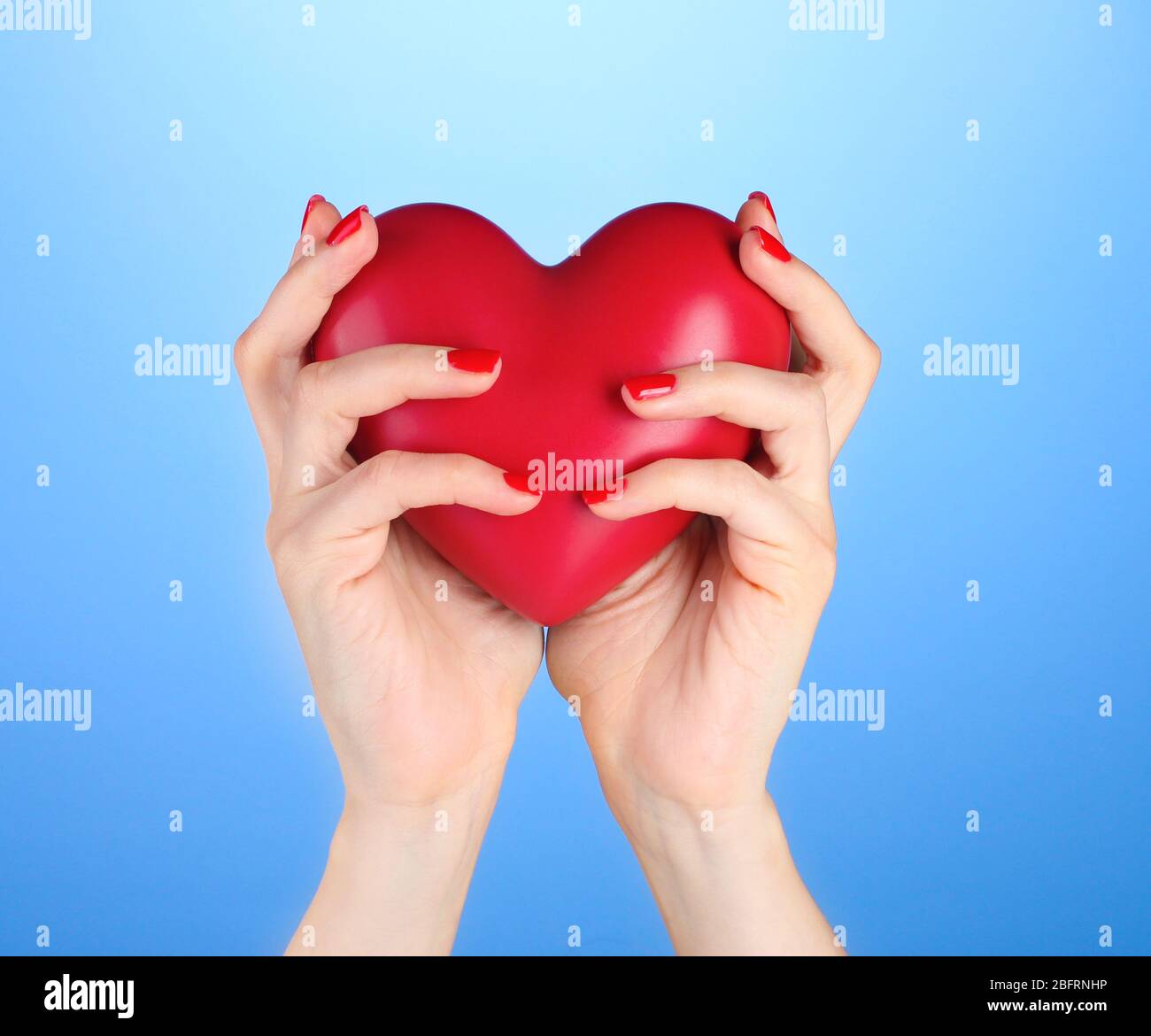 Red heart in woman's hands on blue background Stock Photo - Alamy