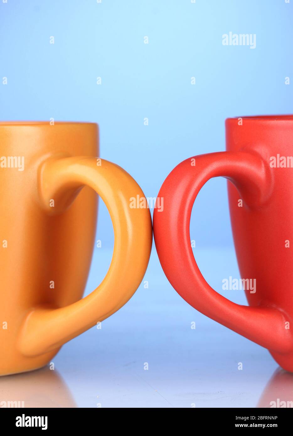 Two colored cups handles close-up on blue background Stock Photo