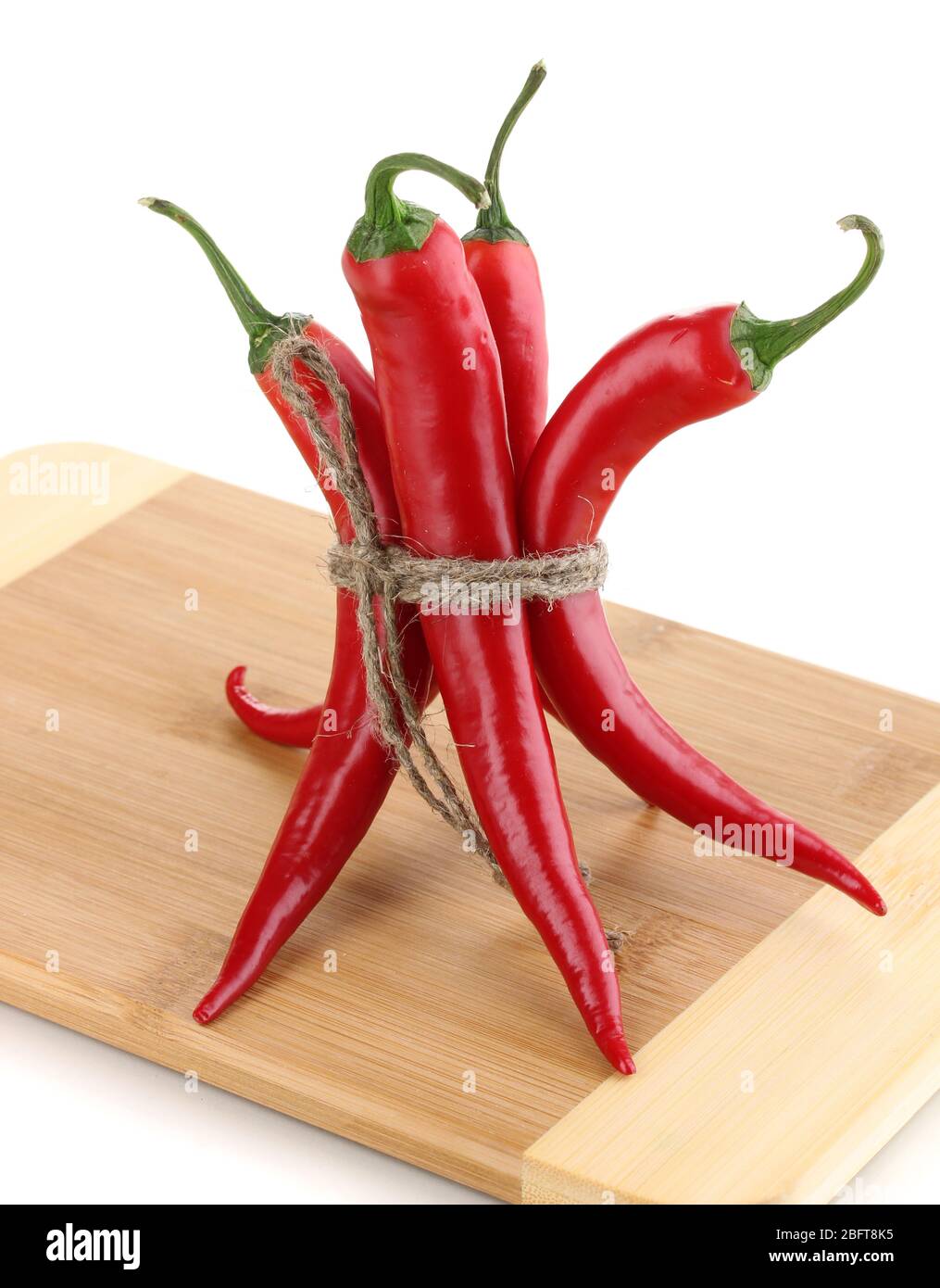 Red hot chili peppers tied with rope on wooden plank isolated on white ...