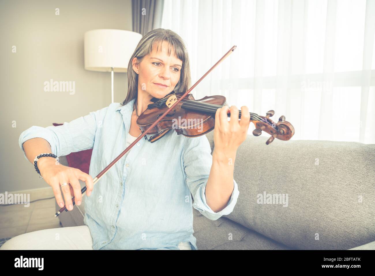 Mature woman playing violin in her urban apartment Stock Photo