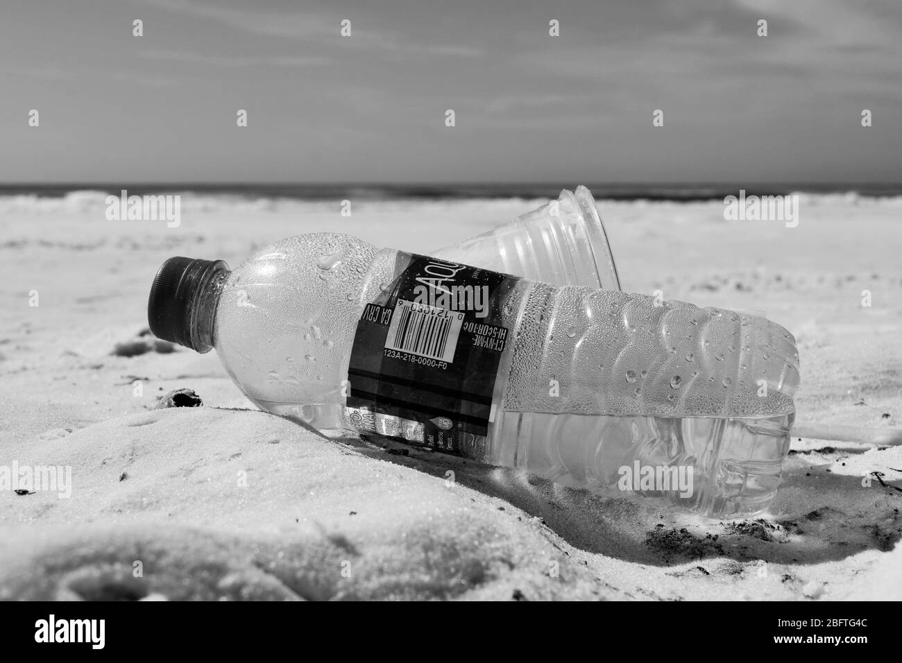 plastic bottles on beach with ocean in background in black and white Stock Photo