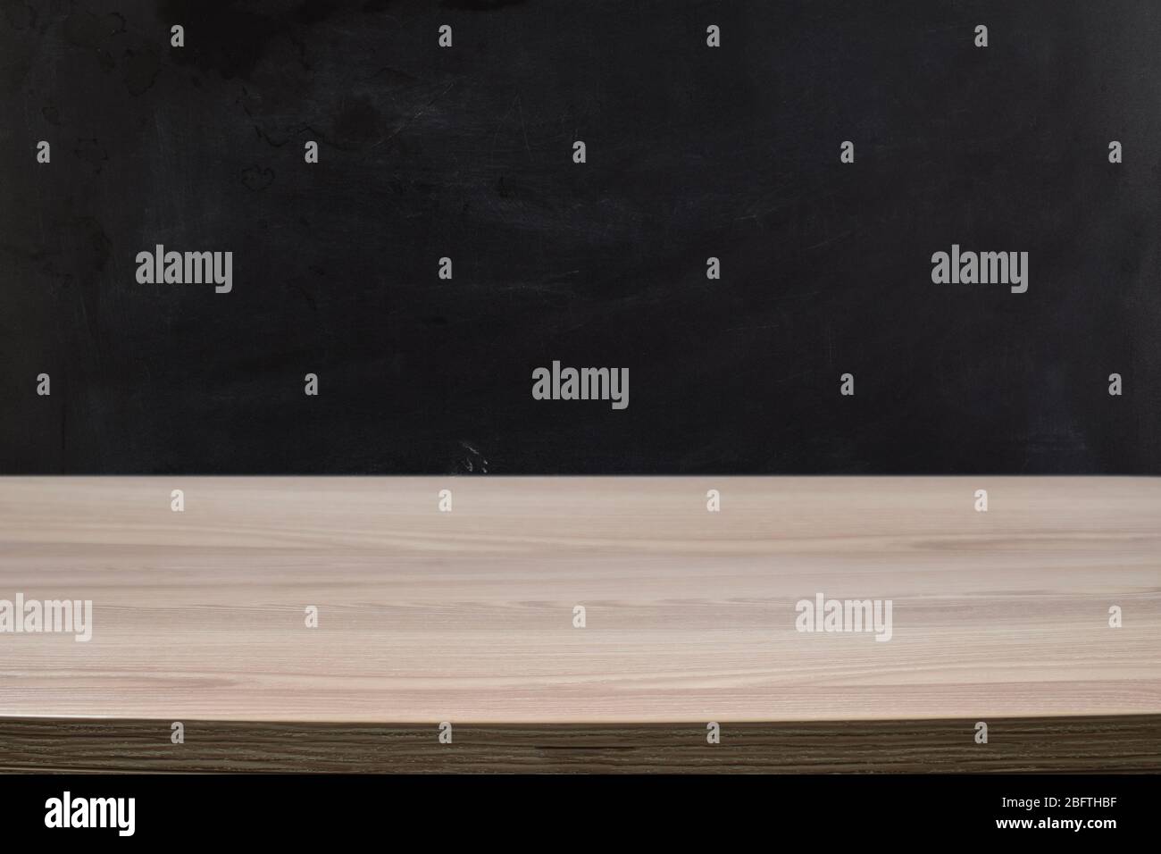 Light wood table against a black chalkboard wall. Stock Photo