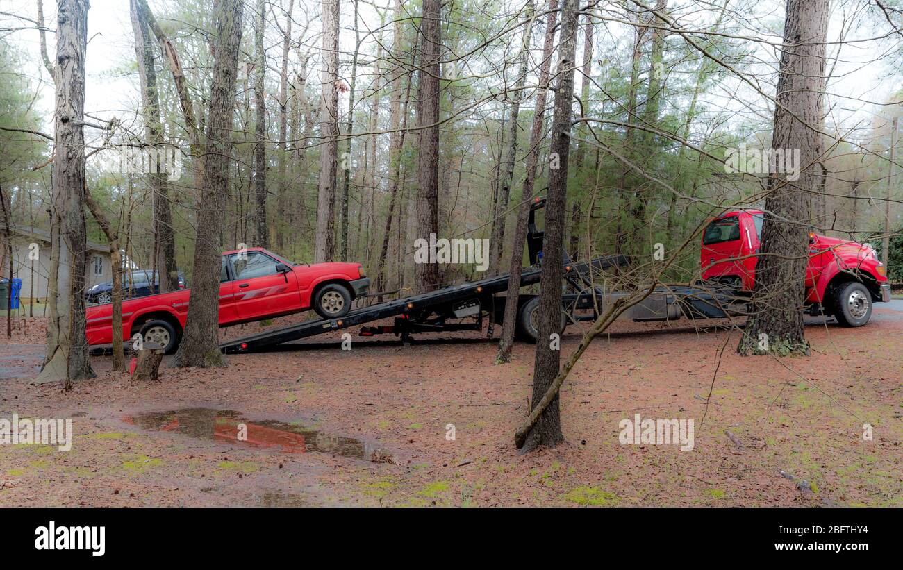 Red pickup truck being loaded on red tilt bed tow truck to be hauled