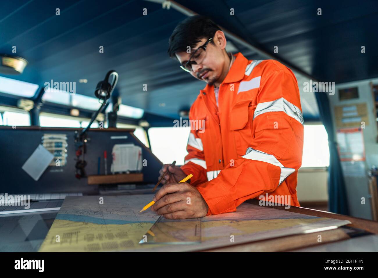 Filipino deck Officer on bridge of vessel or ship. He is plotting position on chart Stock Photo