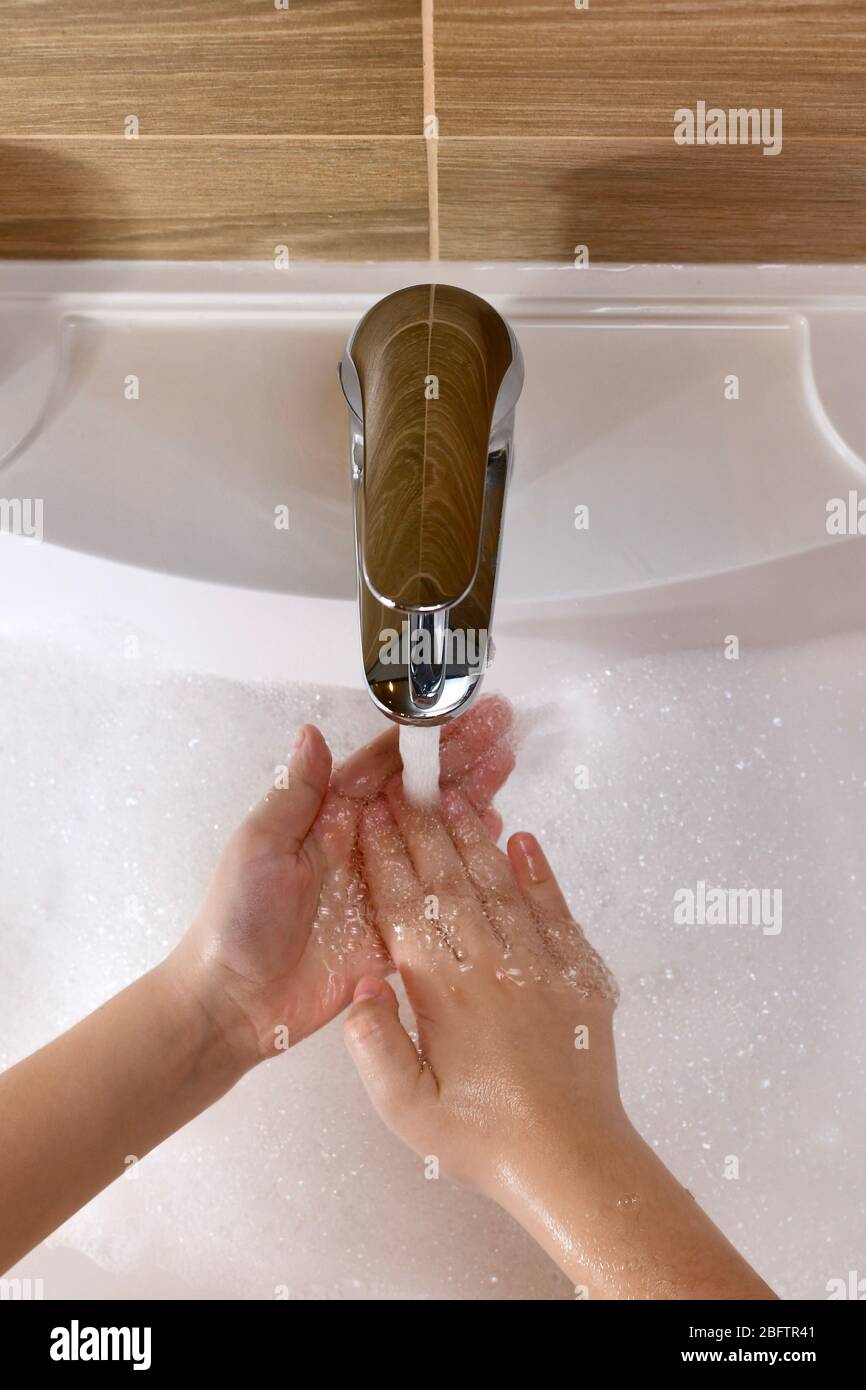 The child learns to wash the inside of the palm in the center with water in the sink.  Stock Photo