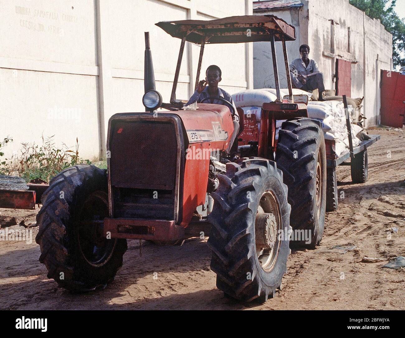 1993 - A Somali man drives a tractor pulling a trailer full of supplies at the food storage warehouse in Kismayo.  After the food is accounted for, it is delivered to food distribution centers throughout the city by United Nations Forces in Somalia in support of  OPERATION CONTINUE HOPE. Stock Photo