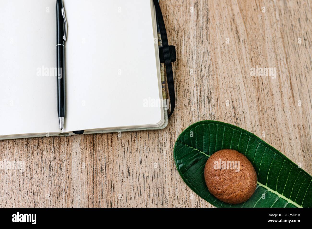 Notepad with white paper, unfolded, lies on a wooden background, a pen on the back of a notebook. chocolate cookies for breakfast. top view, flat lay, Stock Photo