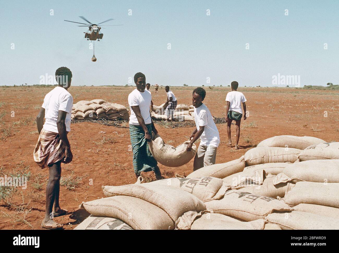 1993 - Men from the village of Maleel stack bags of wheat as a Marine Heavy Helicopter Squadron 363 (HMH-363) CH-53D Sea Stallion helicopter prepaers to drop another load during the multinational relief effort OPERATION RESTORE HOPE. Stock Photo