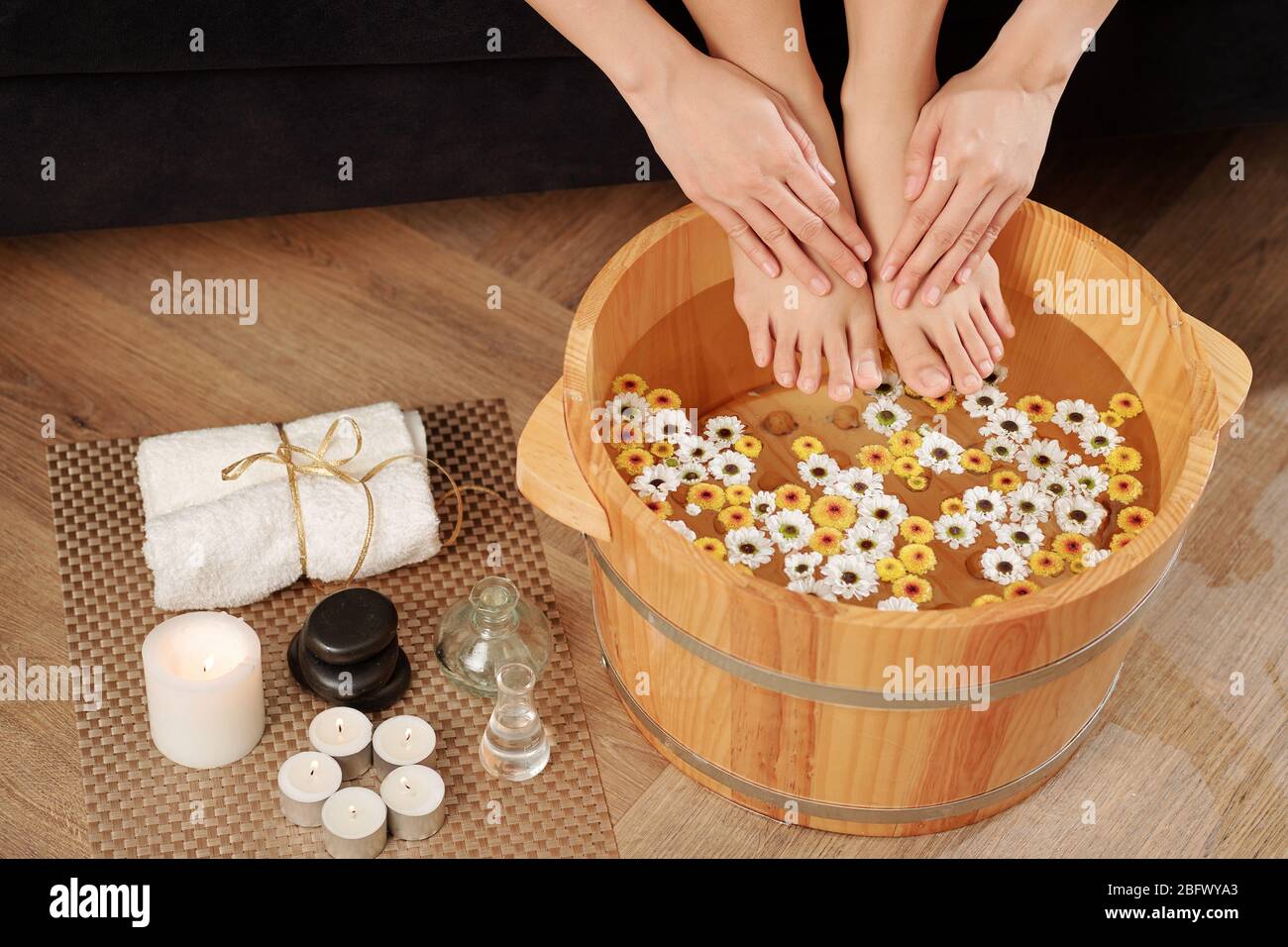 Woman putting feet and hands in wooden basin with flower infused water