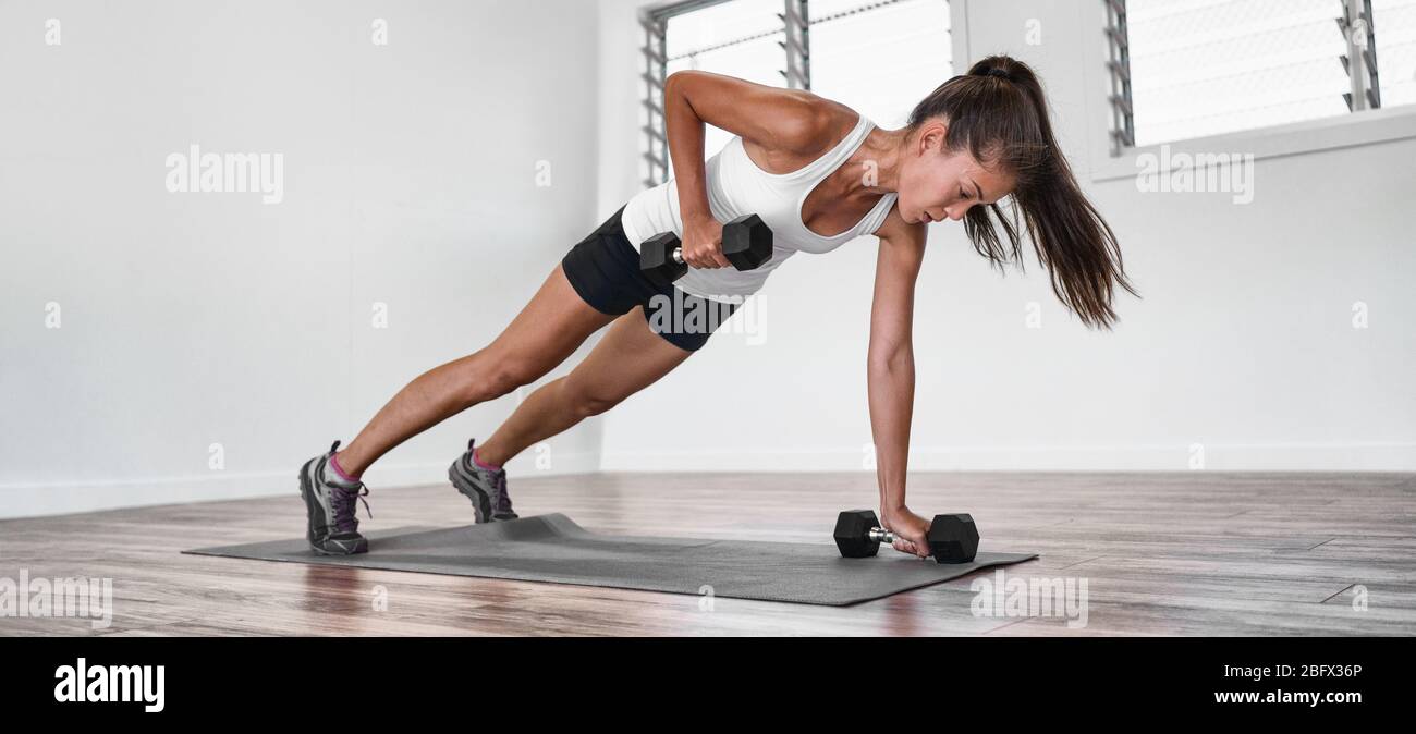 Home fitness plank row workout Asian woman training arms doing rowing exercise planking with dumbbell weights inside. one arm row exercising indoors. Panoramic banner. Stock Photo