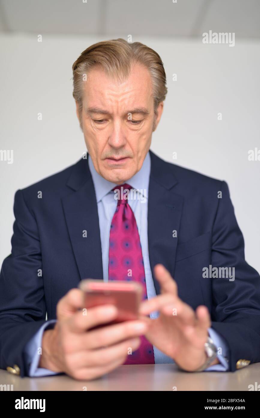 Mature handsome businessman in suit using phone at work Stock Photo - Alamy