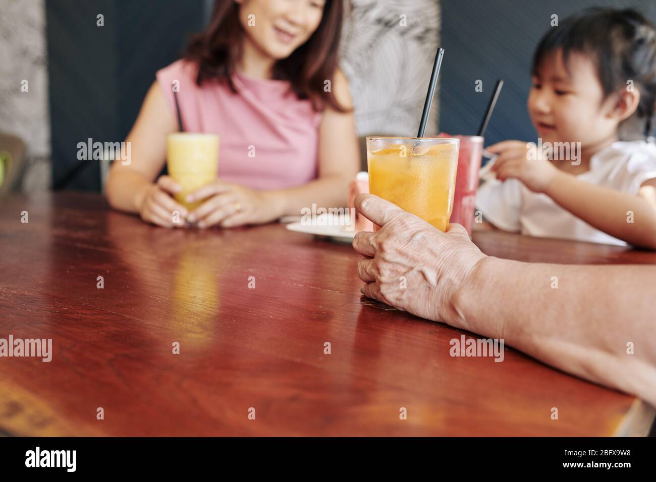 Hand of senior woman drinking fruit cocktail when celebrating birthday of her little granddaughter in cafe Stock Photo