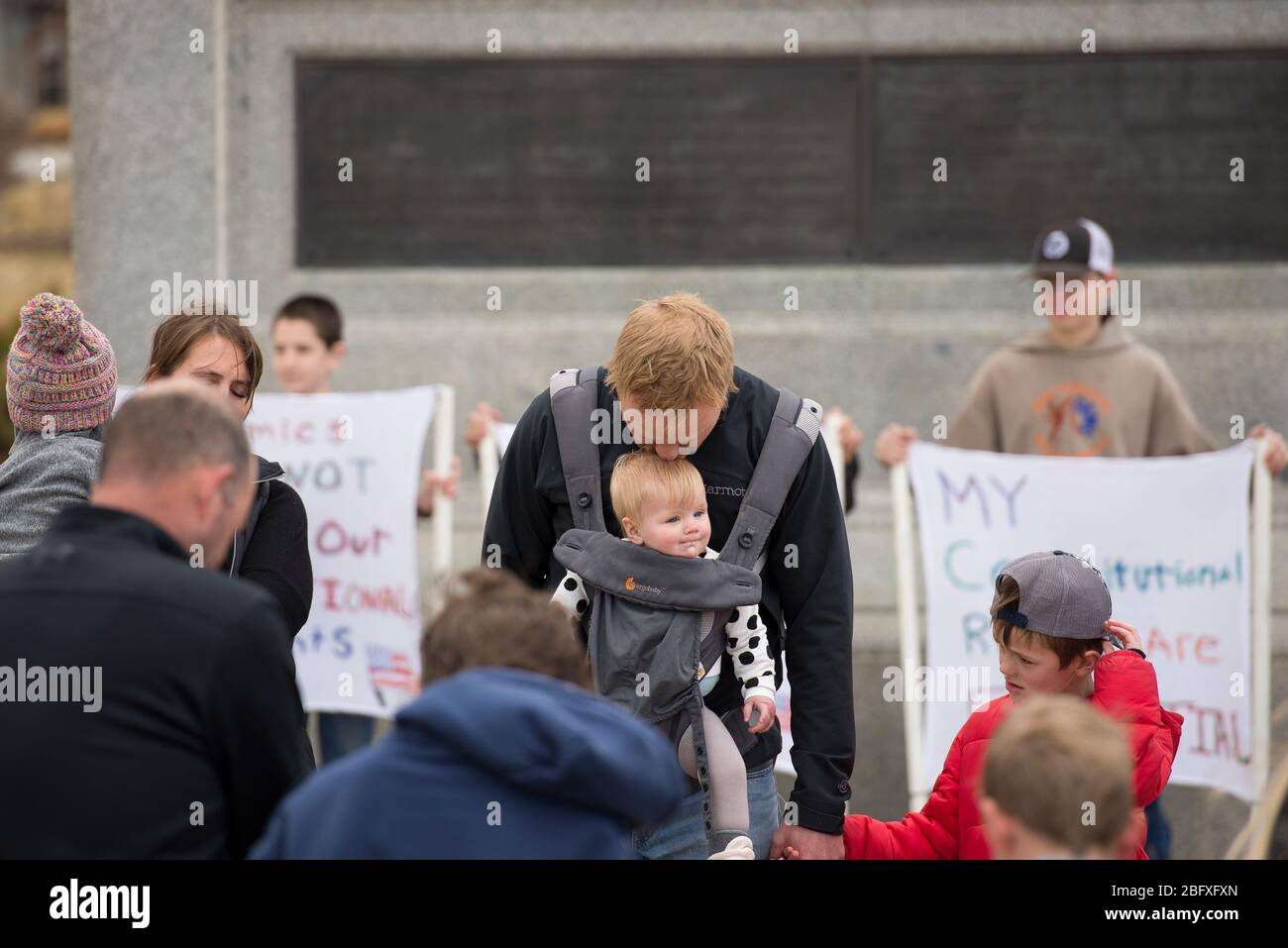 Helena, Montana - April 19, 2020: Man and father kissing baby on head while praying at a protest over the stay at home orders and government shutdown Stock Photo