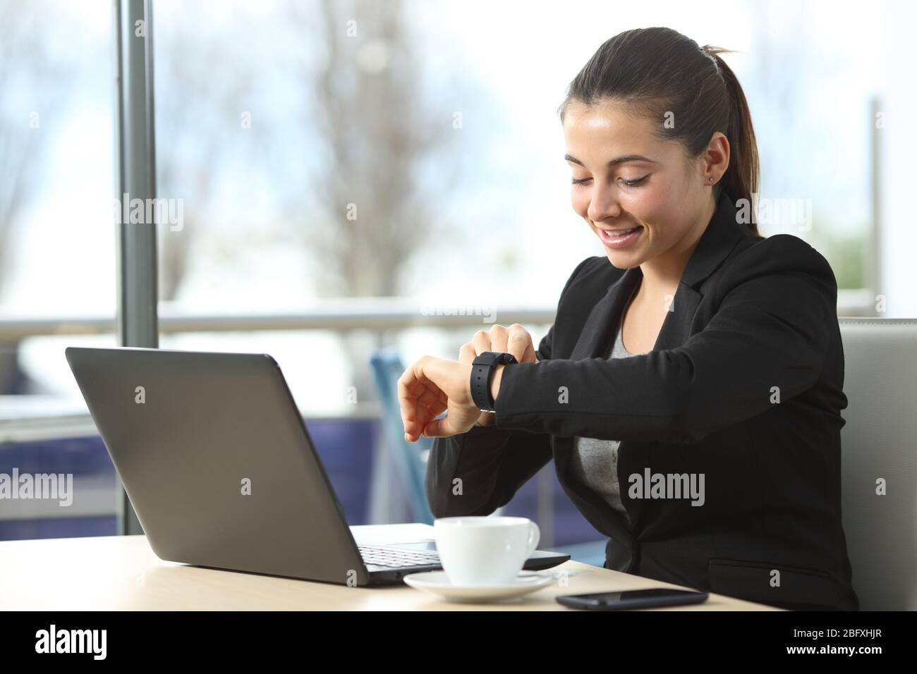 Happy entrepreneur woman checking smartwatch sitting in a coffee shop Stock Photo