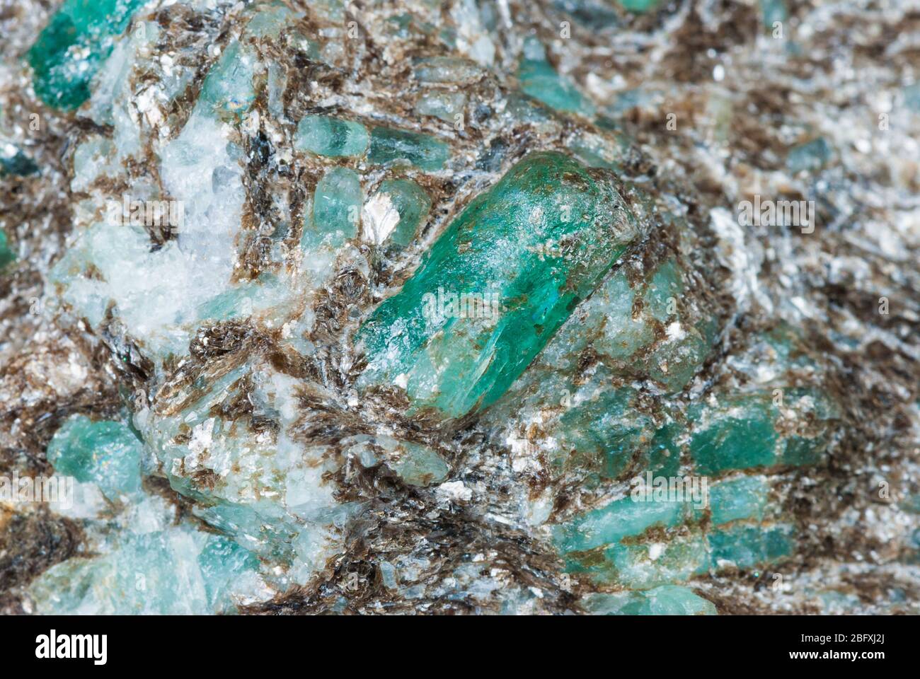 Many dissolved green emerald crystals in a matrix of shiny mica flakes. The beryl mineral is an ore of beryllium used for the production of tank armor Stock Photo