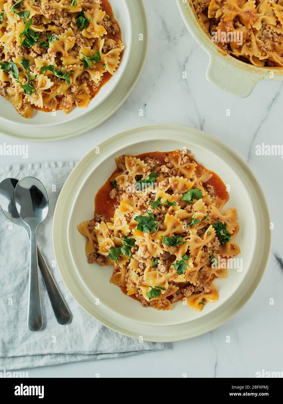 Pasta Farfalle with tomato sauce and ground meat in plate on white marble tabletop. Idea and recipes for easy, simple lunch or dinner one-pot meat goulash. Top down view or flat lay. Vertical Stock Photo