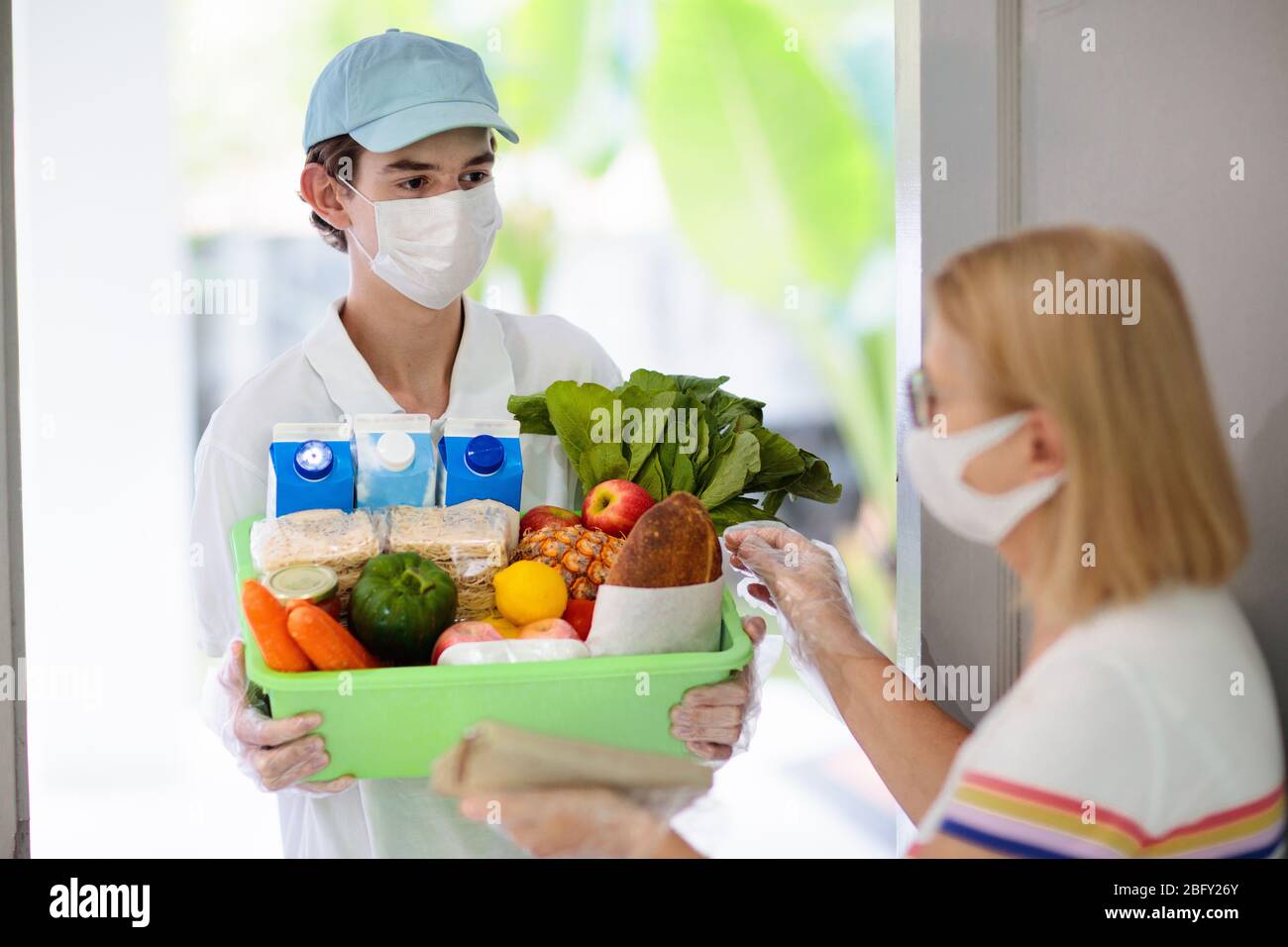Food delivery during corona virus outbreak. Courier wearing face mask delivering grocery order in coronavirus epidemic. Safe shopping in pandemic. Tak Stock Photo
